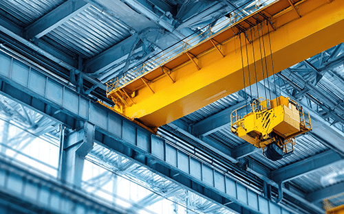 Pont roulant industriel jaune &eacute;quip&eacute; d'un palan et d'une cabine de commande, install&eacute; sous la charpente m&eacute;tallique d'une usine