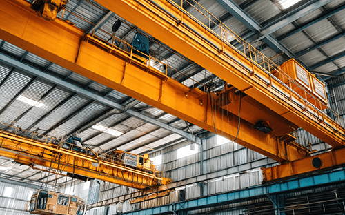 Deux ponts roulants orange install&eacute;s sous la charpente m&eacute;tallique d&rsquo;un vaste atelier industriel