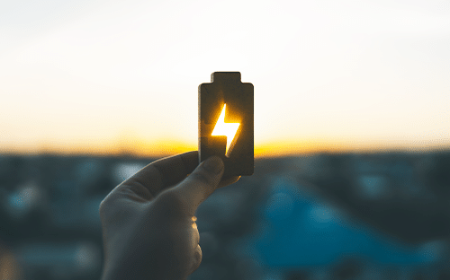 Main tenant un symbole de batterie &eacute;clair&eacute; au coucher du soleil pour illustrer le stockage d&rsquo;&eacute;nergie