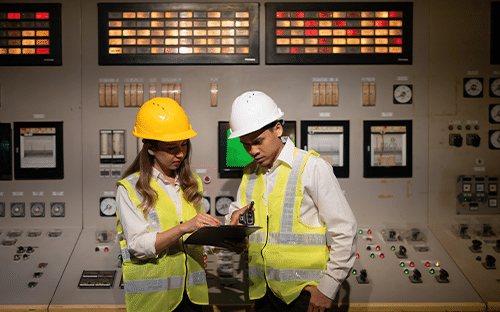 Deux techniciens en équipements de sécurité consultent une tablette devant le pupitre de contrôle d’une installation industrielle